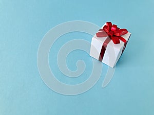White gift box red ribbon bow on blue background, copy space.