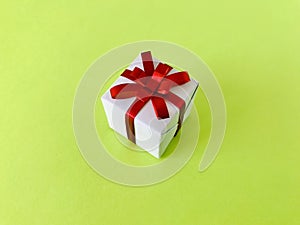 White gift box red ribbon bow on green background.