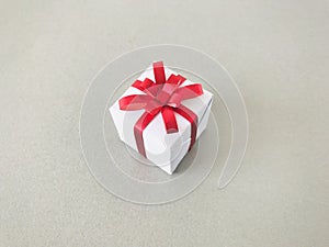 White gift box red ribbon bow on grey background.