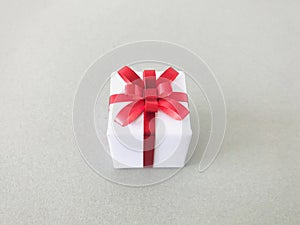 White gift box red ribbon bow on grey background. center.