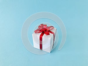 White gift box red ribbon bow on light blue background.