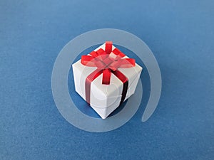 White gift box red ribbon bow on navy blue background. Side view.