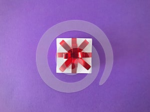 White gift box red ribbon bow on purple background, aerial view.