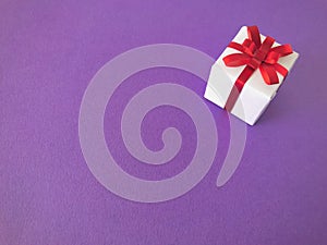 White gift box red ribbon bow on purple background, copy space.