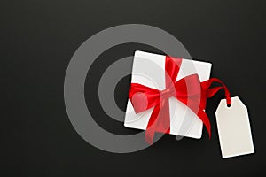 White gift box with red ribbon with sale tag isolated on black background