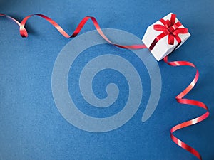 White gift box tied with red ribbon spiral on blue background.