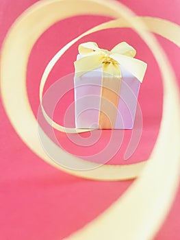 White Gift box at the end of the spiral yellow ribbon, pink background, vertical.