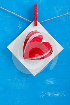 White gift card wih paper hearts on blue wooden background.
