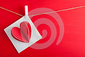 White gift card wih paper hearts on red wooden background.