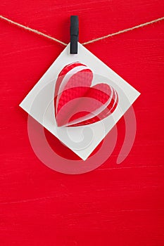 White gift card wih paper hearts on red wooden background.