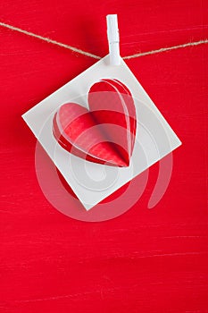 White gift card wih paper hearts on red wooden background.