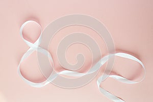 White gift celebration ribbon in 8 digit shape over pink background