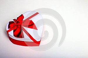 White gift in the form of a heart with a red bow on a white background close-up. Place to insert text