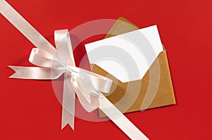 White gift ribbon bow diagonal on red paper background with blank message card