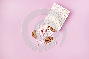 White Gift Shopping Paper Bags Full of Marshmellow and Sweet Cookies and Candy Cane on Pink Background Shopping or Food Holiday