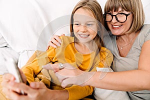 White girl and her grandmother using mobile phone while sitting on sofa