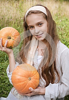 White girl  holding 2 ripe round orange pumpkins on a green background