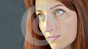 White girl with red hair and green eyes with eyelash extensions on dark background seriously looking up