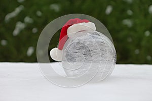 white glass ball on snow with christmas hat. winter world near Christmas tree. snowy background.