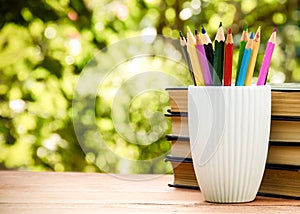 White glass with pencils on green natural background. Stationery and stack of books.