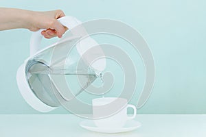 White glass teapot with hot water and drops of condensate.  hand pours hot water into a cup and saucer. Green background