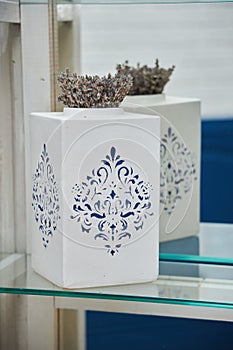 A white glass vase with a blue pattern and a dry plant inside.