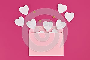 White and golden hearts spilling out of pastel pink envelope on pink background