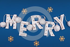 White and golden knitted garland with word MERRY and white pompons on classic blue decorated with golden snowflakes