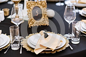 White and golden plates on black tablecloth. Beautiful service of wedding tables.