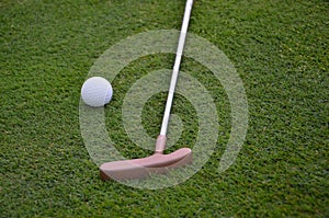 White golf ball and golf club on green grass