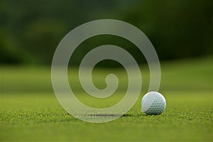 White golf ball near hole on fairway with the green background i