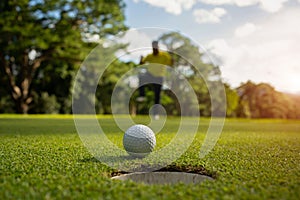 White golf ball rolling down golf hole on putting green with evening golf course backdrop