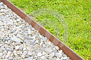 White gravel floor and fresh green lawn with clovers and rusty metal containment profiles