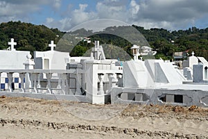 White graves and tombstones in a cemetery near the beach in Castries, Saint Lucia.