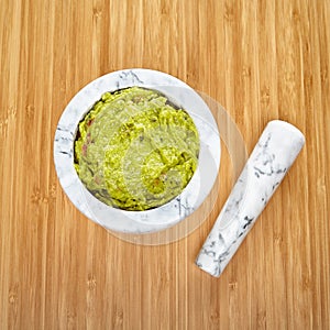 White and gray marble mortar and pestle with guacamole on a bamboo surface