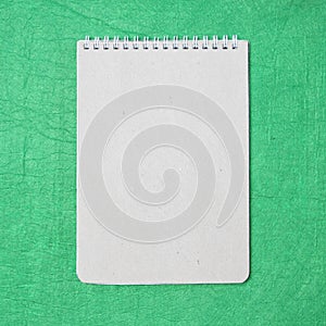 White and gray notepad sheet with spiral against the background of green fabric