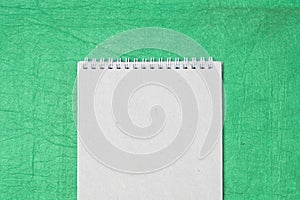 White and gray notepad sheet with spiral against the background of green fabric