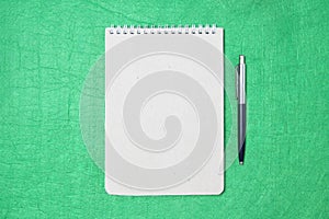 White and gray notepad sheet with spiral with pen against the background of green fabric