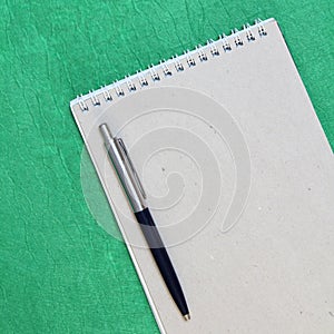 White and gray notepad sheet with spiral with pen against the background of green fabric