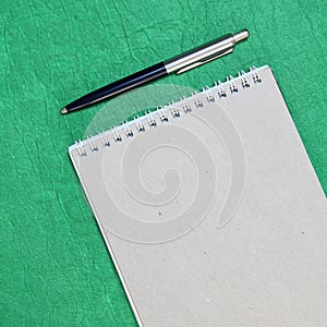 White and gray notepad sheet with spiral with pen against the background of green fabric