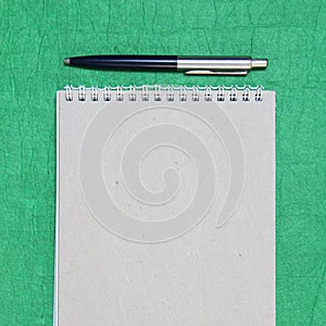 White and gray notepad sheet with spiral with pen against the background of green fabric