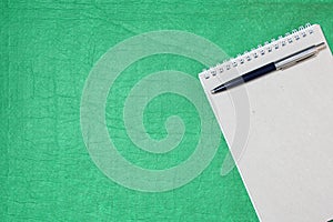 White and gray notepad sheet with spiral with pen against the background of green fabric