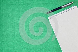 White and gray notepad sheet with spiral with pen against the background of green fabric