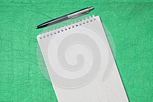 White and gray notepad sheet with spiral with pen against the background of green fabric