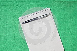 White and gray notepad sheet with spiral with pen against the background of green fabric