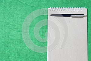 White and gray notepad sheet with spiral with pen against the background of green fabric