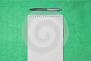 White and gray notepad sheet with spiral with pen against the background of green fabric