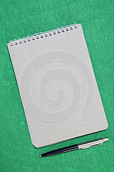 White and gray notepad sheet with spiral with pen against the background of green fabric