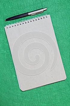 White and gray notepad sheet with spiral with pen against the background of green fabric