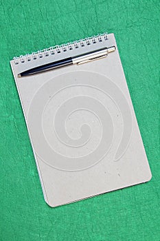 White and gray notepad sheet with spiral with pen against the background of green fabric